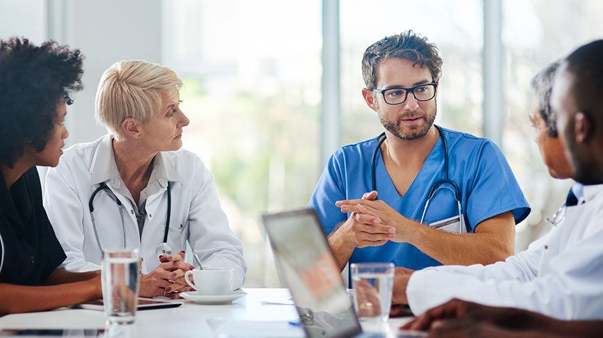 Image of five healthcare professionals conversing while sitting around a table